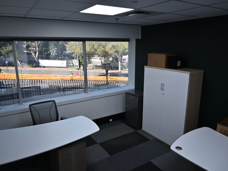 A functional office space featuring large windows with street views, suspended ceilings with recessed lighting, and durable carpet tile flooring.