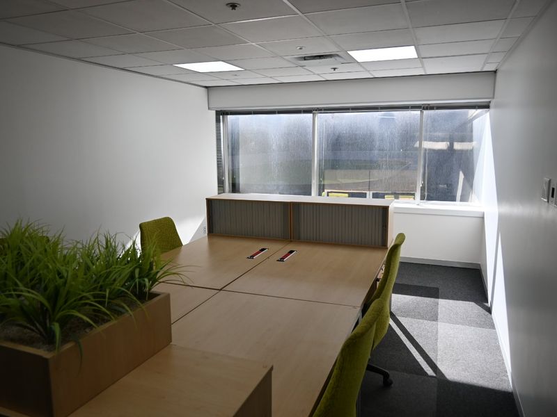 A functional office space featuring a suspended ceiling, recessed lighting, carpeted flooring, and a large window providing natural light.