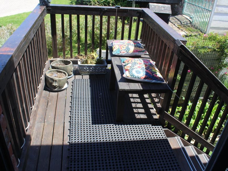 A compact timber balcony featuring a wooden balustrade and staircase, overlooking a garden area.
