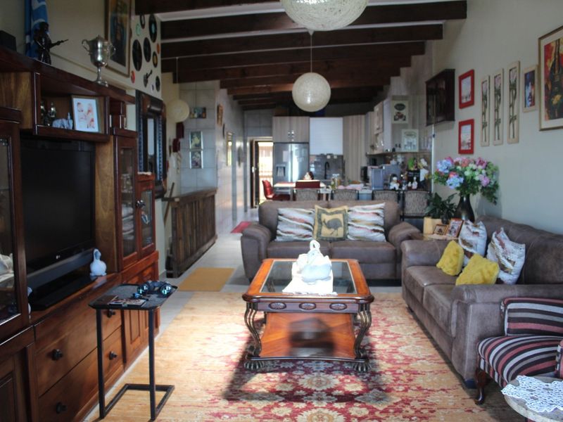 Open-plan living area featuring exposed timber ceiling beams, tiled flooring, and a connected kitchen space with built-in cabinetry.