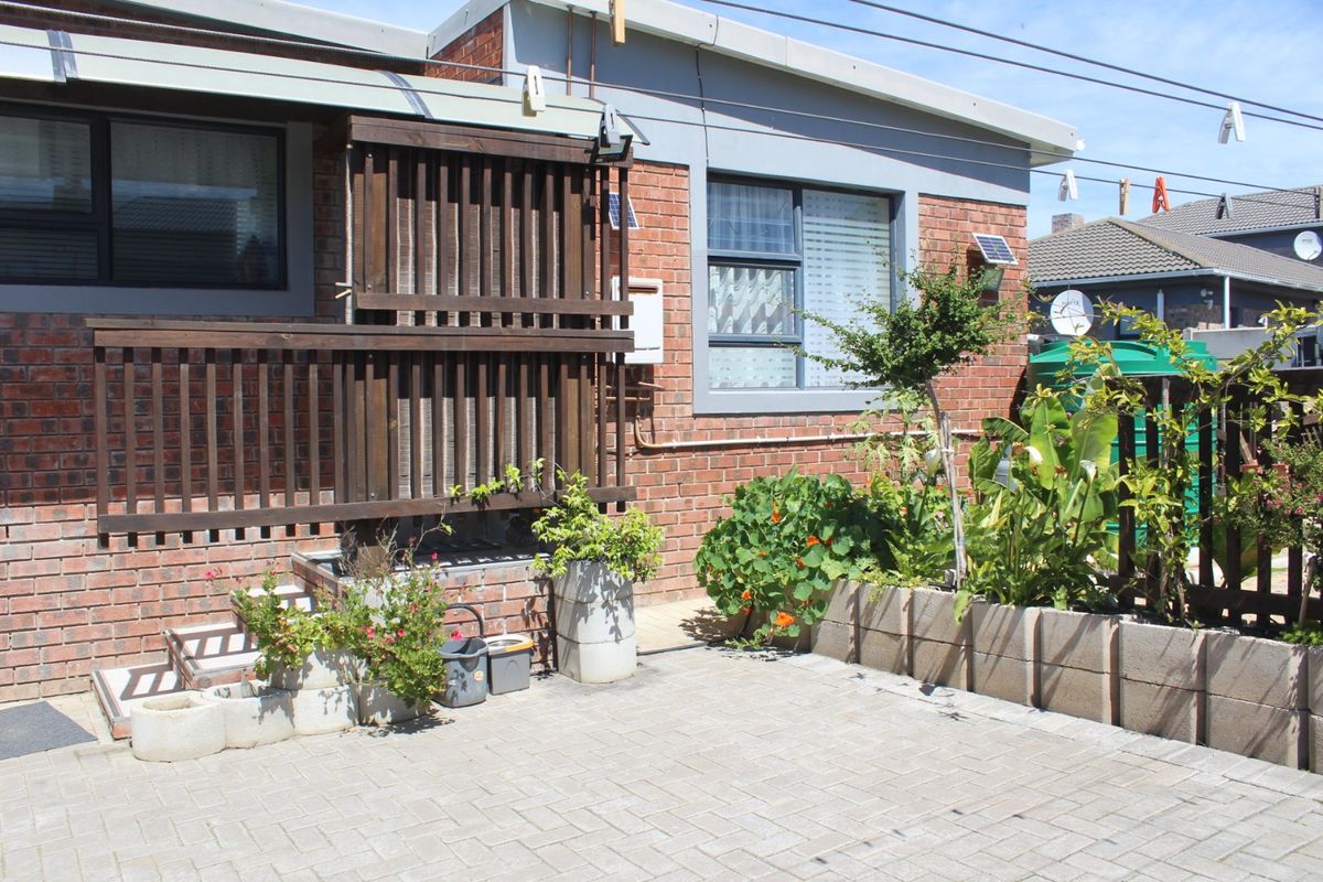 Rear exterior view featuring a paved patio area, brick facade, and a timber privacy screen with integrated garden planters.