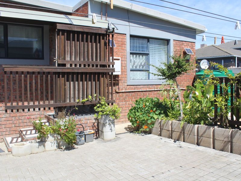 Rear exterior view featuring a paved patio area, brick facade, and a timber privacy screen with integrated garden planters.