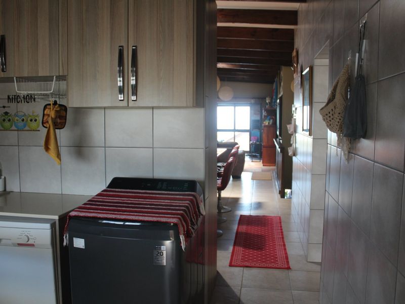 A kitchen area featuring built-in cabinetry, tiled walls, and tiled flooring, with a view leading through to the living space under exposed timber ceiling beams.