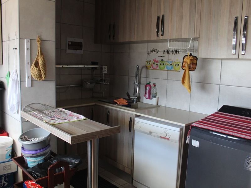 A functional scullery area featuring built-in cabinetry, laminate countertops, a stainless steel sink, and tiled splashbacks, providing practical utility space.