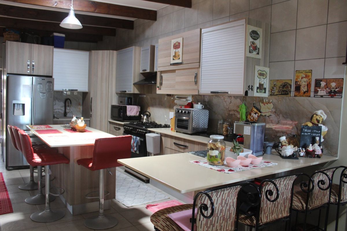 A functional kitchen featuring built-in cabinetry, a central island, gas stove, extractor fan, and exposed timber ceiling beams with tiled finishes throughout.