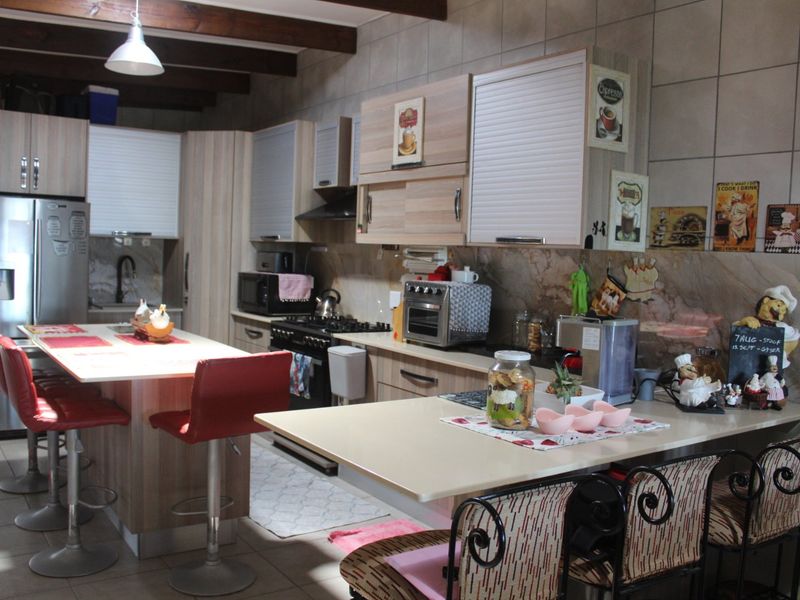 A functional kitchen featuring built-in cabinetry, a central island, gas stove, extractor fan, and exposed timber ceiling beams with tiled finishes throughout.
