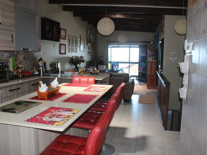 Open-plan kitchen and living area featuring a central island, tiled flooring, and exposed timber ceiling beams, creating a functional and connected living space.