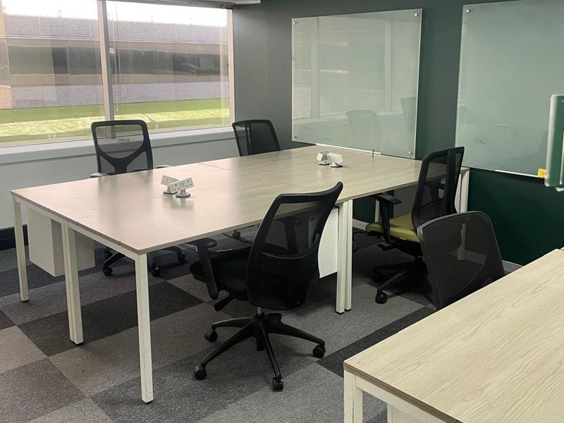 A professional office space featuring large windows for natural light, glass whiteboards, and durable carpet tiles, suitable for a collaborative work environment.