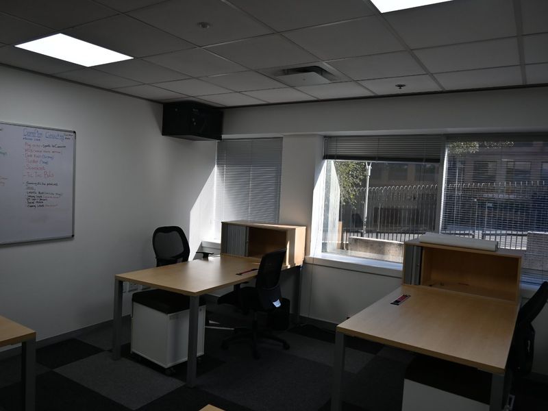A functional commercial office space featuring carpeted flooring, suspended ceiling with recessed lighting, and large windows providing natural light.