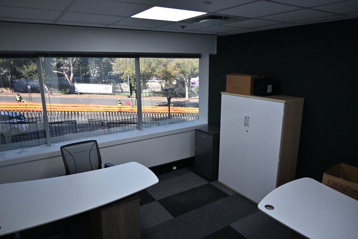 A functional office space featuring large windows with street views, suspended ceilings with recessed lighting, and durable carpet tile flooring.