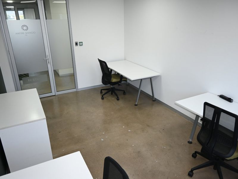A functional commercial office space featuring polished concrete flooring and a modern glass entry door, providing a clean and professional work environment.