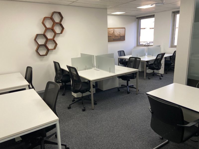 A functional commercial office space featuring carpeted flooring, suspended ceilings with recessed lighting, and multiple workstations with integrated privacy dividers.