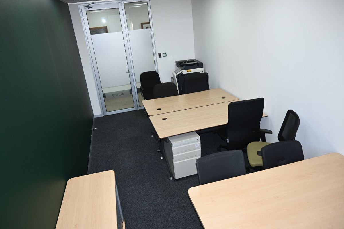 A functional office space featuring dark carpet flooring, white walls, and a glass-paneled entrance door, suitable for a professional work environment.