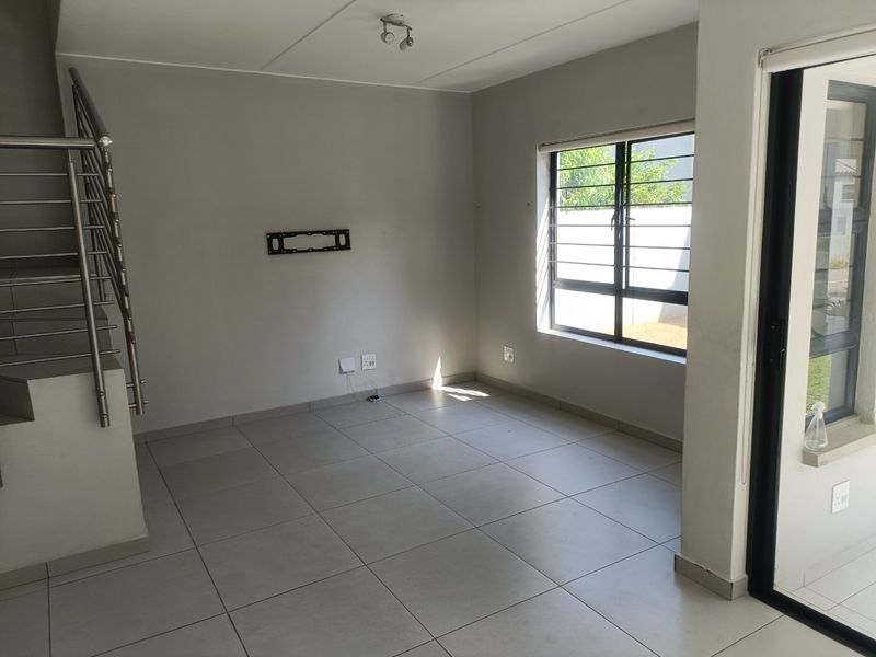 An empty, open-plan living area featuring neutral tiled flooring, a modern stainless steel staircase balustrade, and direct access to an outdoor space via sliding doors.