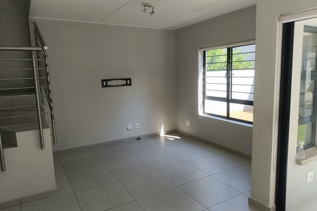 An open-plan living area featuring neutral tiled flooring, a modern staircase with a stainless steel balustrade, and access to the exterior via a sliding door.