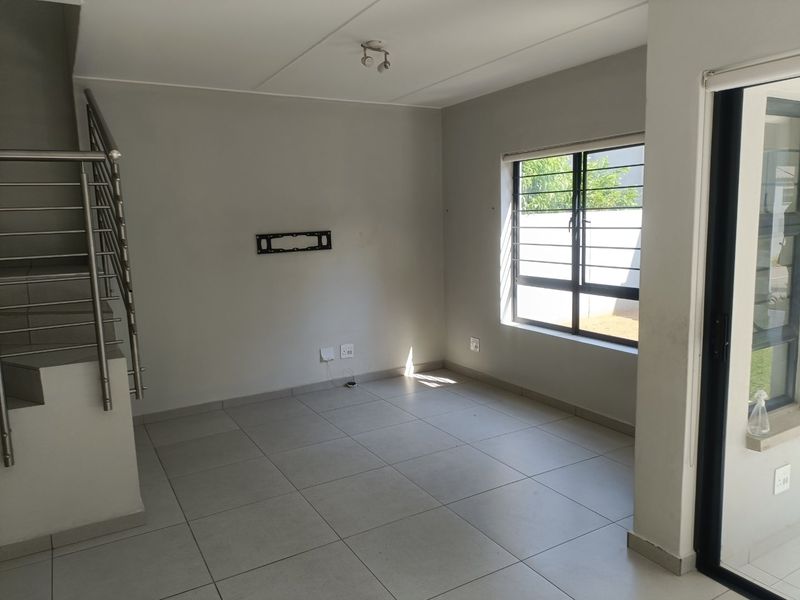 An open-plan living area featuring neutral tiled flooring, a modern staircase with a stainless steel balustrade, and access to the exterior via a sliding door.