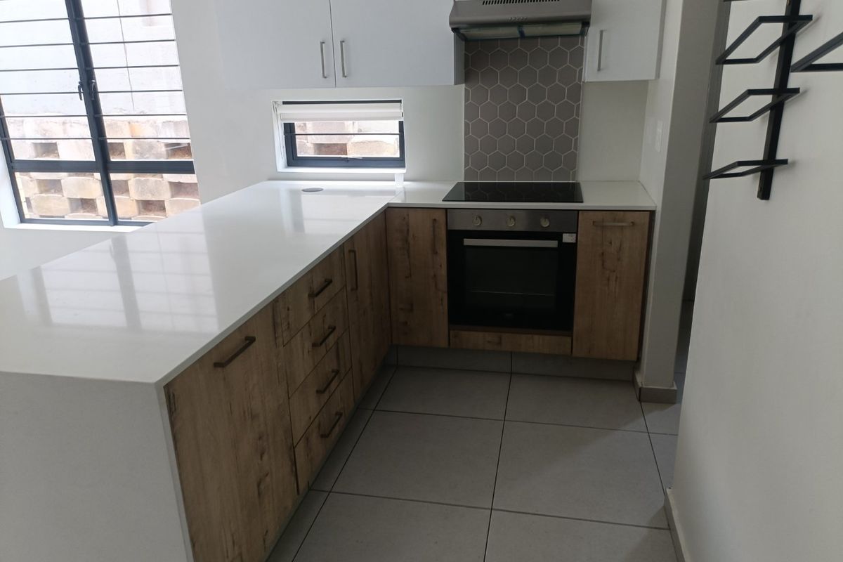 Modern kitchen featuring quartz countertops, built-in oven, electric hob, extractor fan, and stylish hexagonal tile backsplash with ample storage cabinetry.
