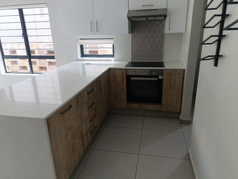 Modern kitchen featuring quartz countertops, built-in oven, electric hob, extractor fan, and stylish hexagonal tile backsplash with ample storage cabinetry.