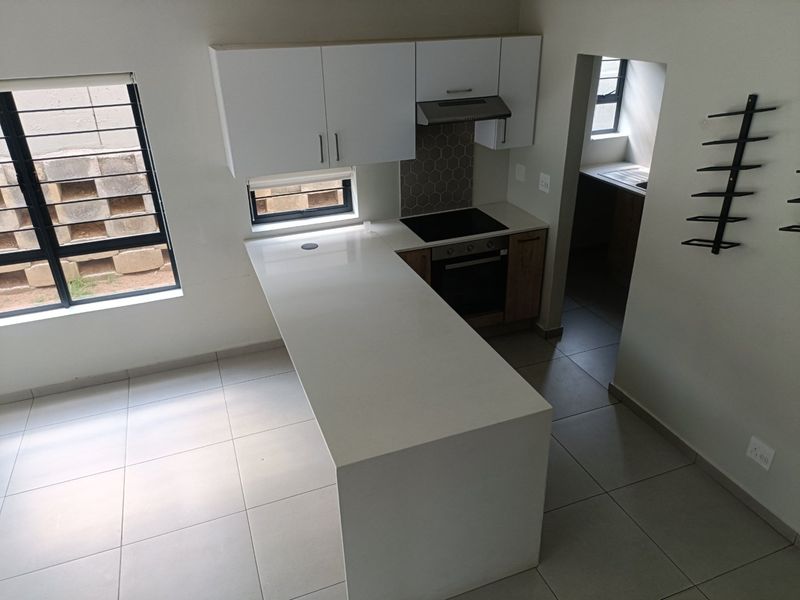 Modern kitchen featuring white cabinetry, stone countertops, integrated electric hob and oven, and a convenient adjoining scullery area with tiled flooring throughout.