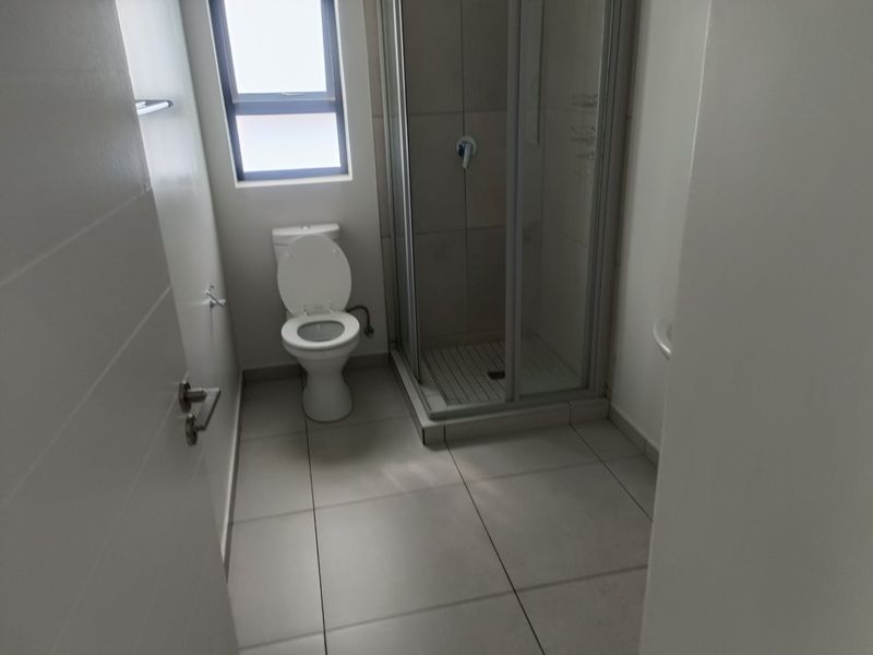 A clean, functional bathroom featuring a shower enclosure, toilet, and neutral floor tiling.