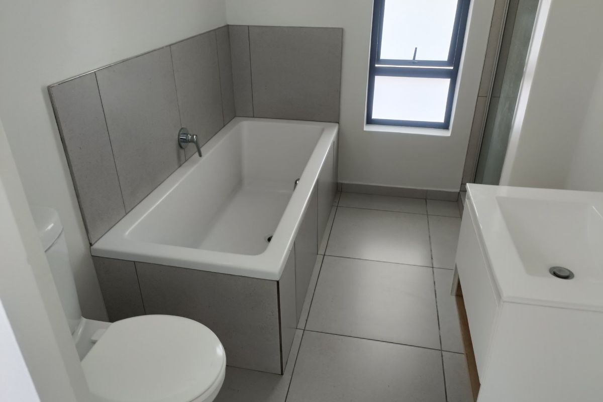 A clean, modern bathroom featuring a built-in bathtub, vanity basin, toilet, and tiled finishes, offering a functional and well-maintained space.