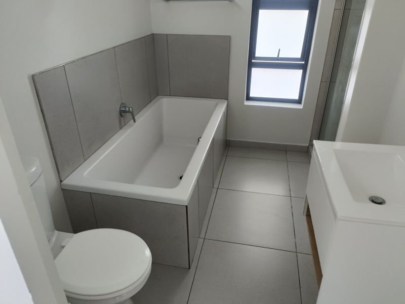 A clean, modern bathroom featuring a built-in bathtub, vanity basin, toilet, and tiled finishes, offering a functional and well-maintained space.