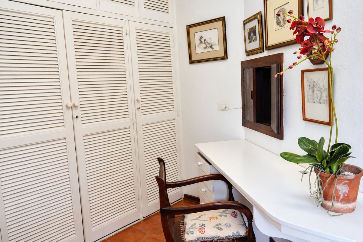 Bedroom featuring built-in louvered wardrobes, a fitted desk area, and terracotta floor tiles.