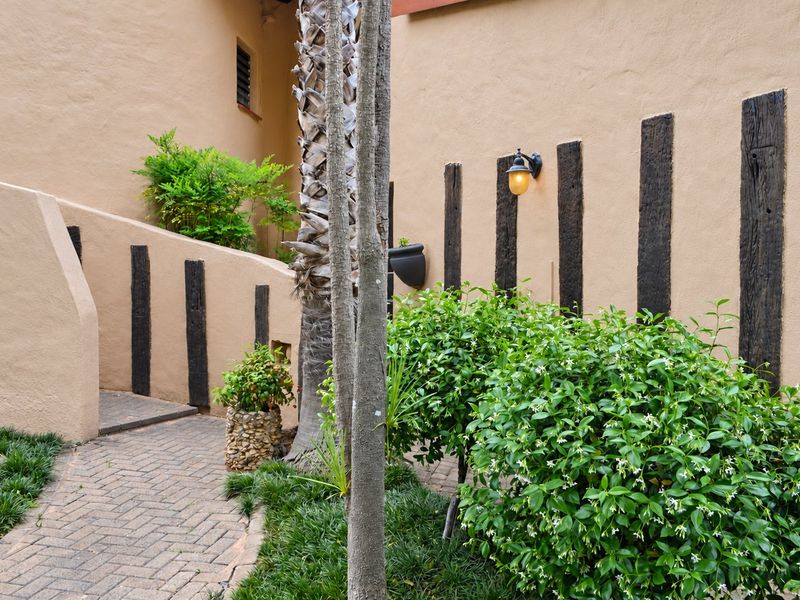 A well-maintained rear exterior area featuring a brick paved pathway, textured stucco walls with decorative timber accents, and integrated wall lighting.