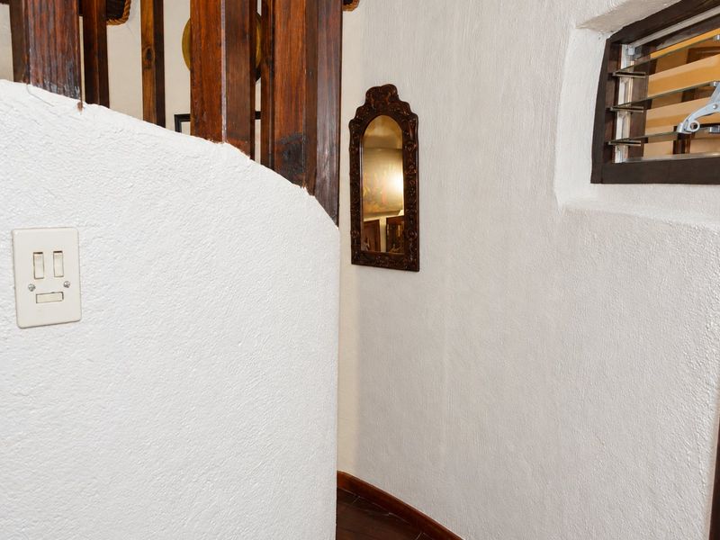 A hallway featuring textured white walls, a wooden staircase balustrade, and a louvered window, showcasing a dated but functional interior space.