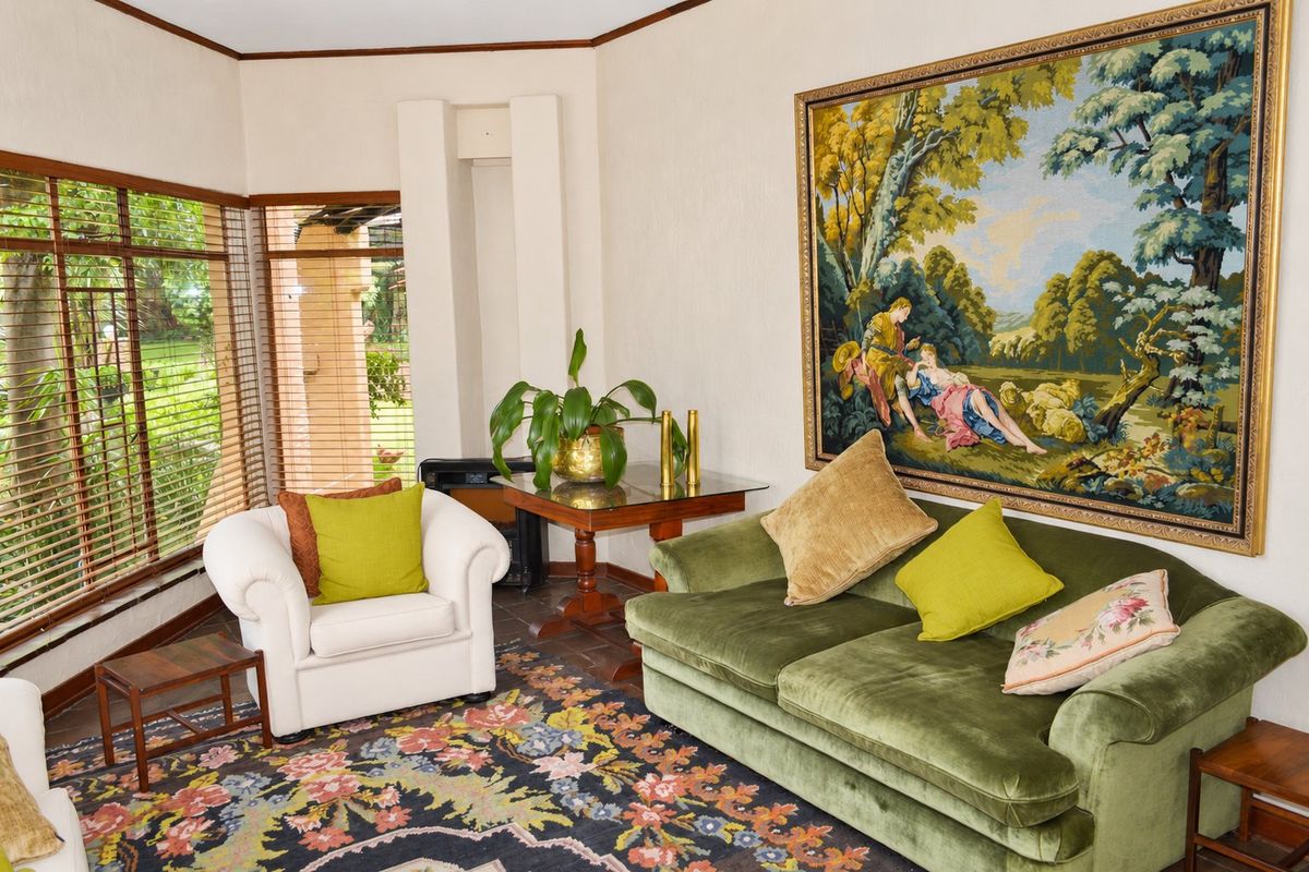 A comfortable living room featuring corner windows with timber blinds, tiled flooring, and a neutral wall finish.