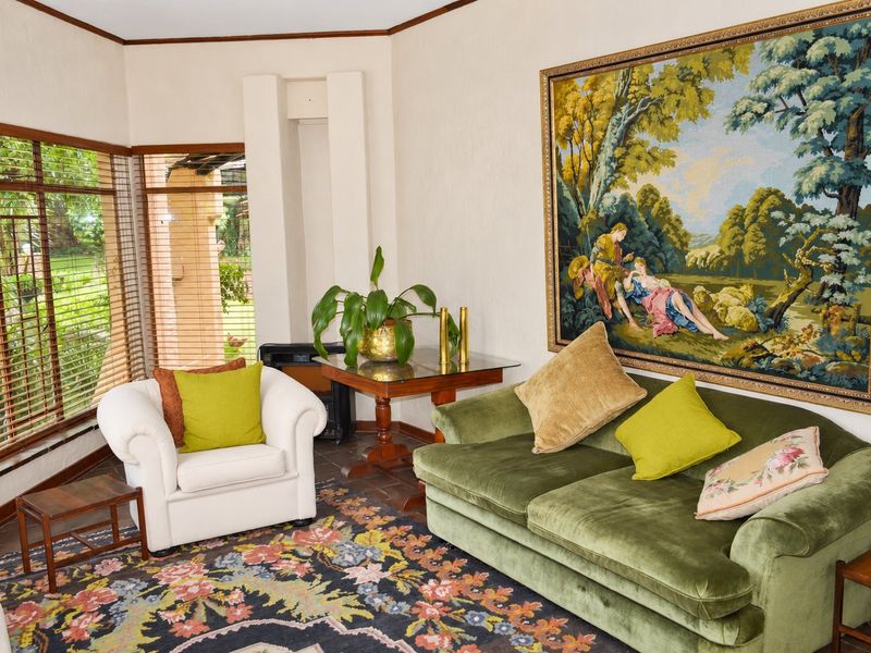 A comfortable living room featuring corner windows with timber blinds, tiled flooring, and a neutral wall finish.