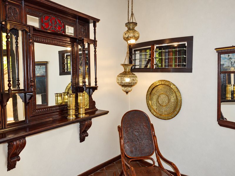 A well-maintained hallway featuring ornate wooden wall mirrors, decorative brass pendant lighting, and terracotta floor tiles.