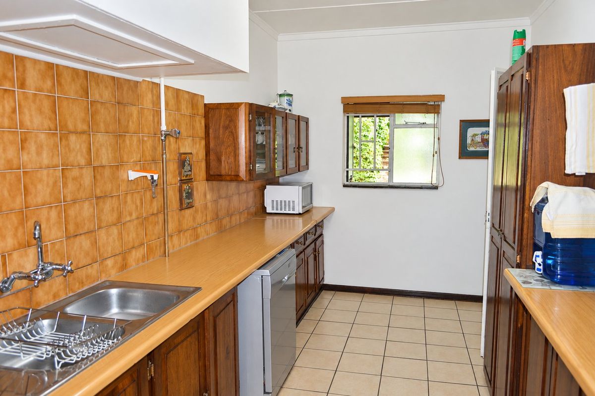 A functional kitchen featuring wooden cabinetry, laminate countertops, a stainless steel sink, and tiled finishes, offering a classic layout with potential for modern updates.