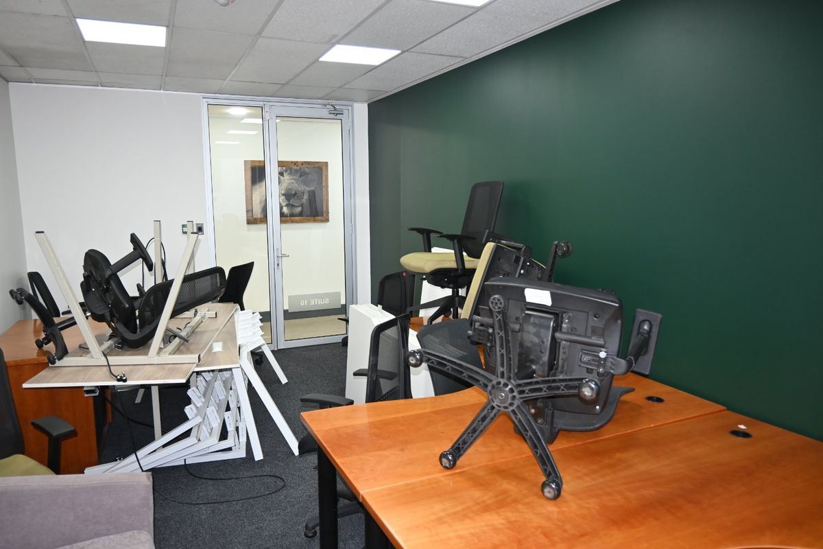 A commercial office space featuring a dark green accent wall, carpeted flooring, suspended ceiling with recessed lighting, and a glass partition door.
