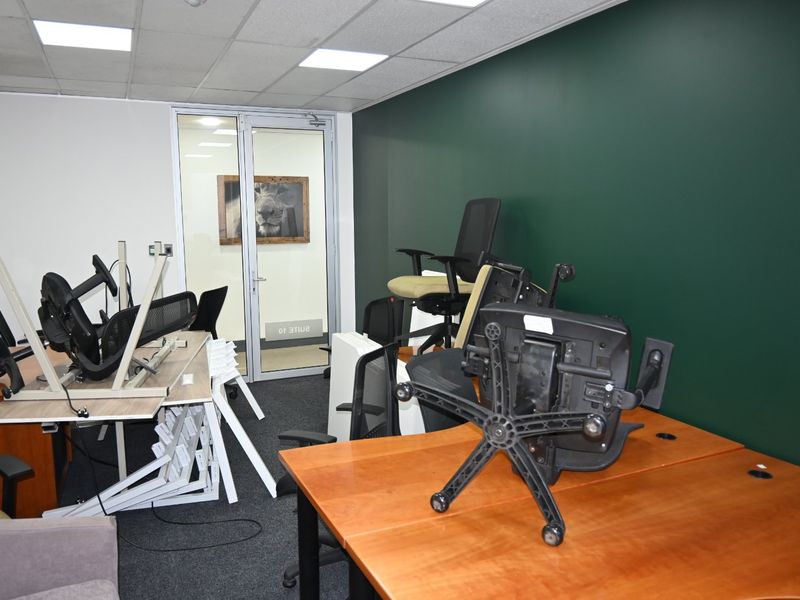 A commercial office space featuring a dark green accent wall, carpeted flooring, suspended ceiling with recessed lighting, and a glass partition door.