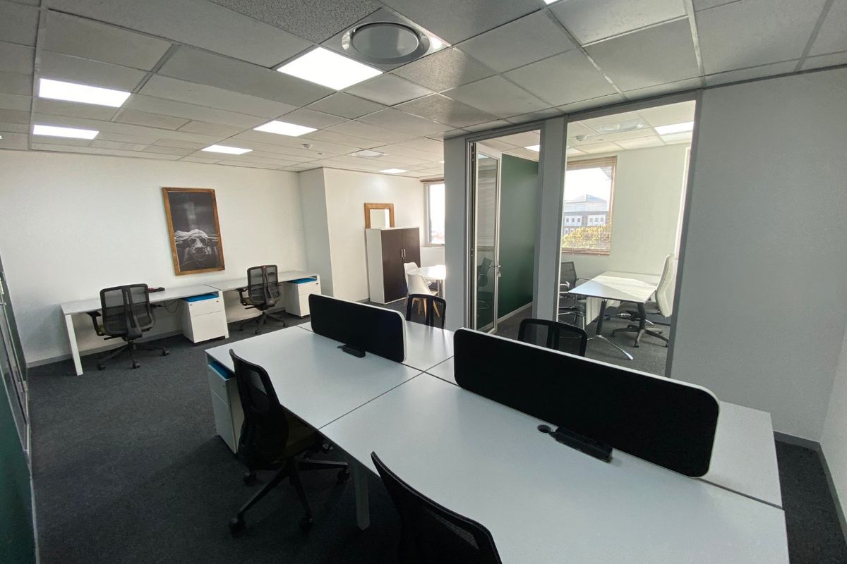 A modern commercial office space featuring glass partitions, suspended ceilings with recessed lighting, and carpeted flooring, providing a professional and functional work environment.