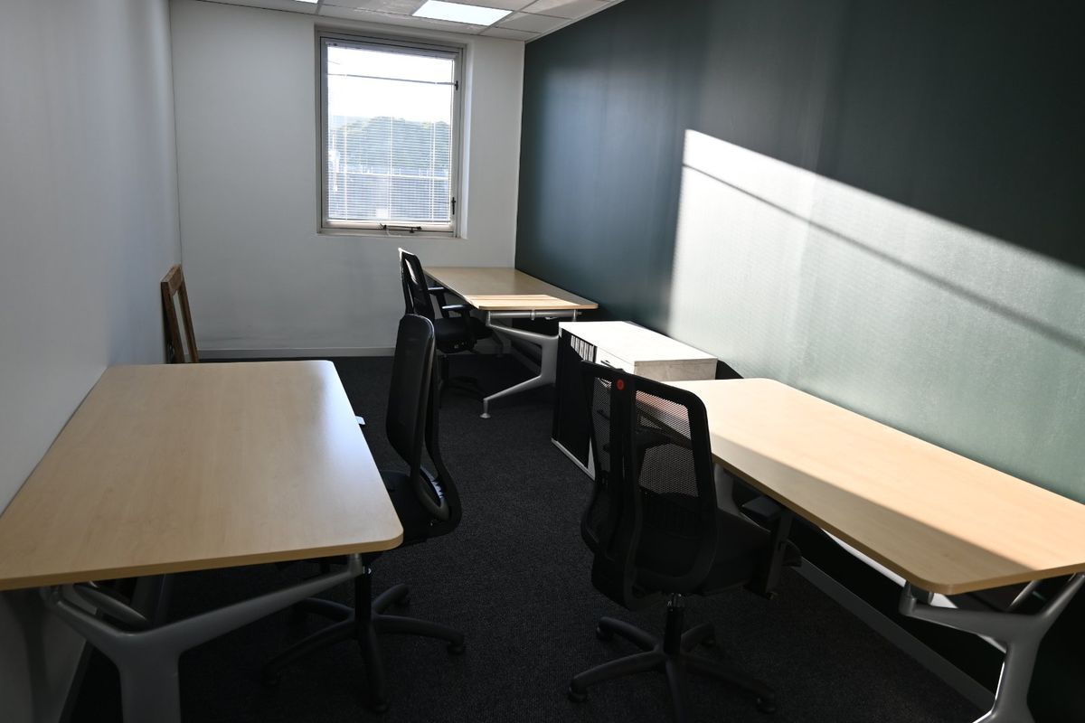 A functional commercial office space featuring dark carpet flooring, a dark accent wall, and recessed ceiling lighting with natural light from a window.