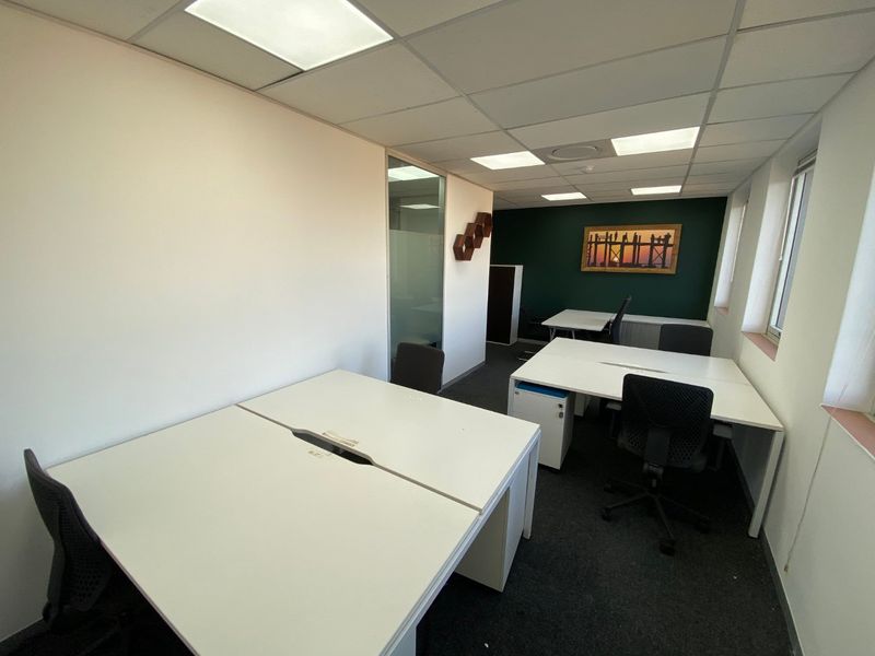 A functional commercial office space featuring a suspended ceiling with recessed lighting, glass partitioning, and dark carpet flooring.