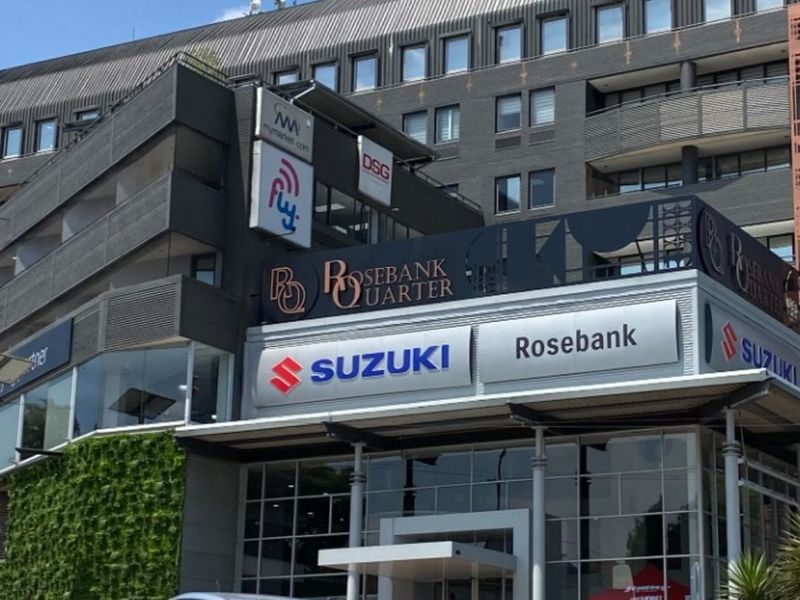 A modern multi-story commercial building featuring a prominent glass-fronted showroom, vertical garden elements, and clear corporate signage for Rosebank Quarter and Suzuki.