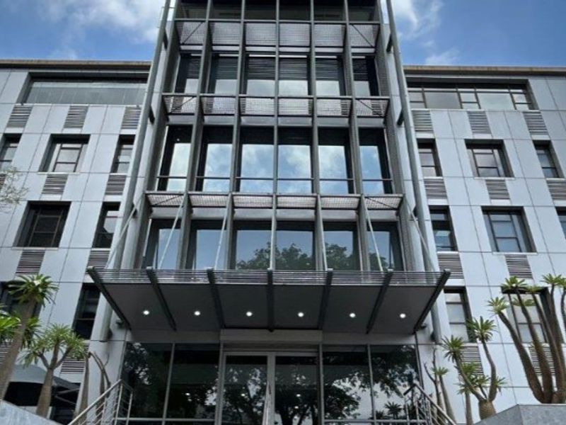 Modern commercial office building facade featuring a glass curtain wall, metal cladding, and a prominent entrance canopy with integrated lighting.