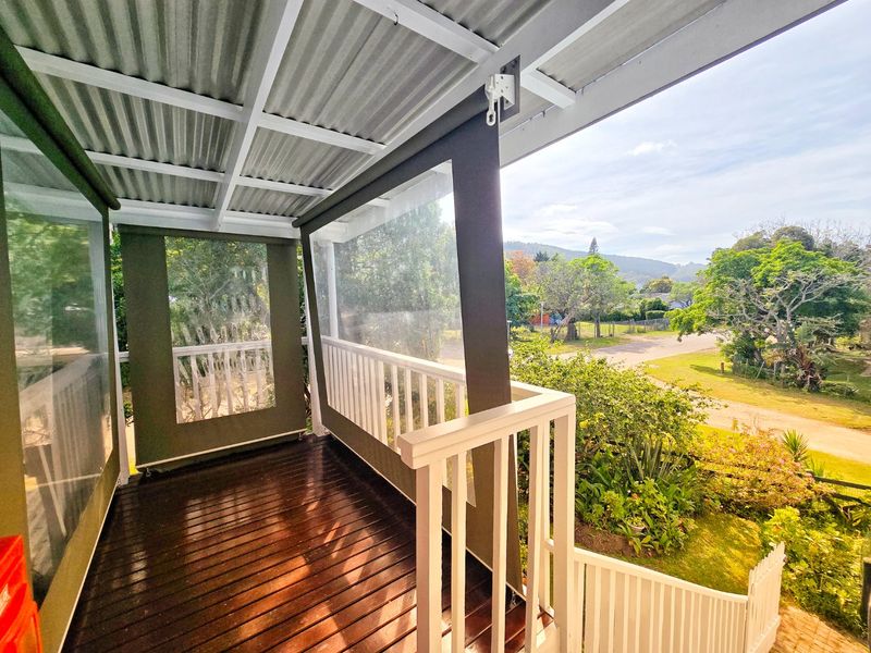 A covered balcony featuring timber decking, white railings, and retractable outdoor blinds, offering an elevated view of the surrounding garden and neighbourhood.