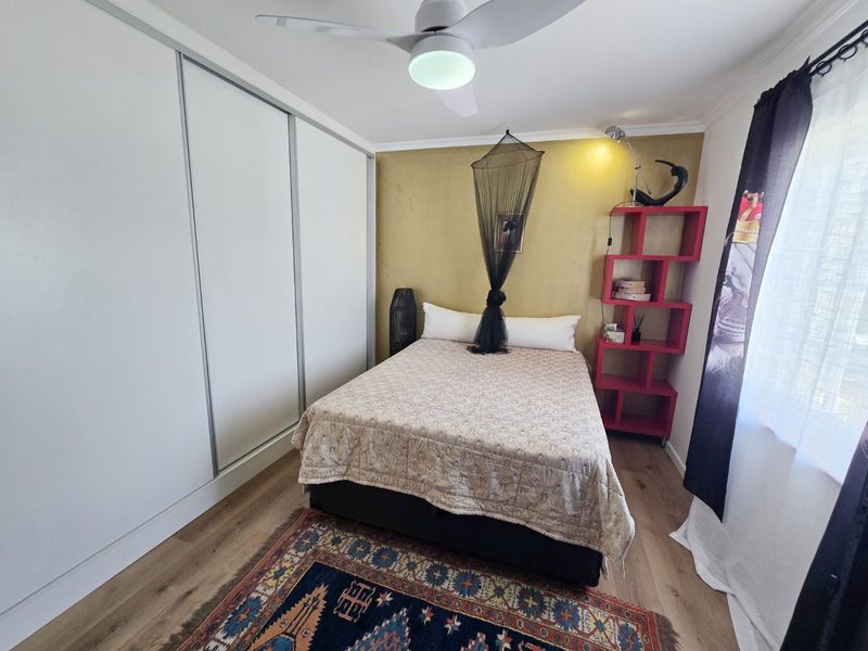 A well-maintained bedroom featuring laminate flooring, a built-in sliding door wardrobe, and a ceiling fan, with a feature wall.
