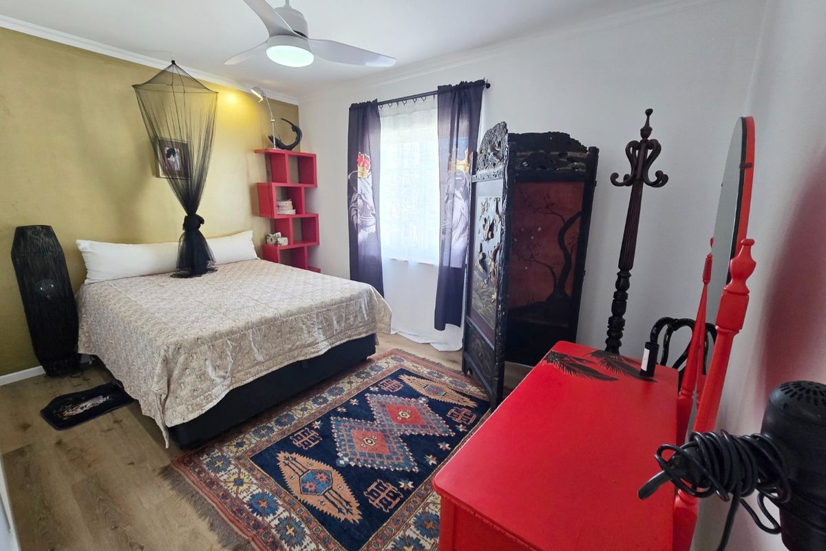 A bedroom featuring laminate flooring, a ceiling fan, and a decorative accent wall, offering a functional space with neutral base finishes.