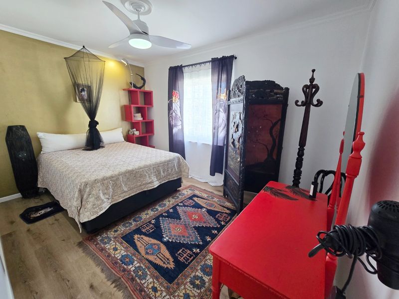 A bedroom featuring laminate flooring, a ceiling fan, and a decorative accent wall, offering a functional space with neutral base finishes.