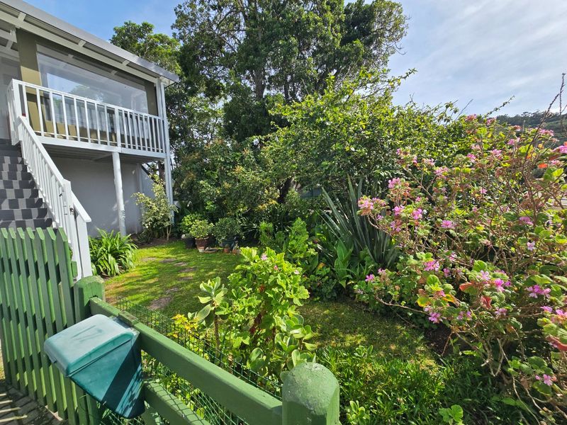 A lush, established garden area featuring a green timber fence, a raised deck with balustrade, and mature landscaping.