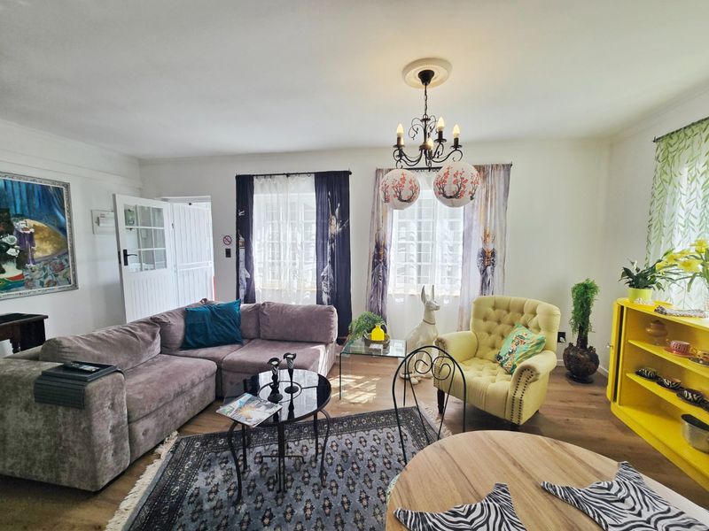 A bright and spacious living room featuring timber flooring, classic multi-pane windows, and a decorative ceiling rose with a chandelier.