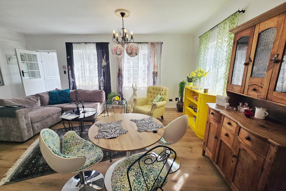A spacious living and dining area featuring laminate flooring, classic multi-pane windows, and a decorative ceiling rose with a central chandelier.