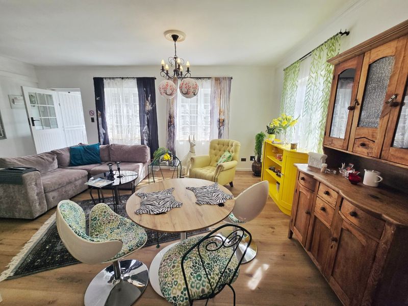 A spacious living and dining area featuring laminate flooring, classic multi-pane windows, and a decorative ceiling rose with a central chandelier.