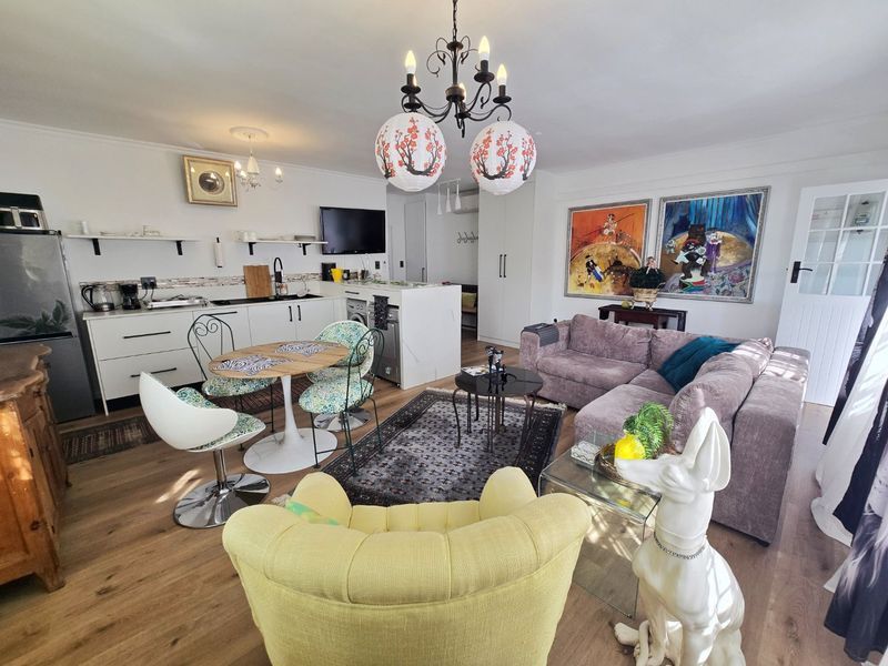An open-plan living and kitchen area featuring modern white cabinetry, laminate flooring, and a functional layout suitable for contemporary apartment living.