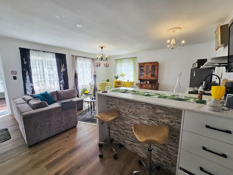Spacious open-plan living area featuring a stone-clad breakfast bar, modern laminate flooring, and integrated kitchen cabinetry with elegant ceiling detailing.